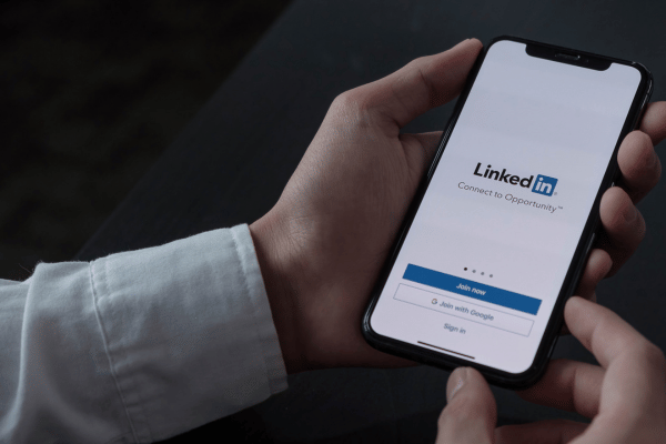 Zu sehen ist eine Person, die ein Smartphone mit der App LinkedIn in der Hand hält.
